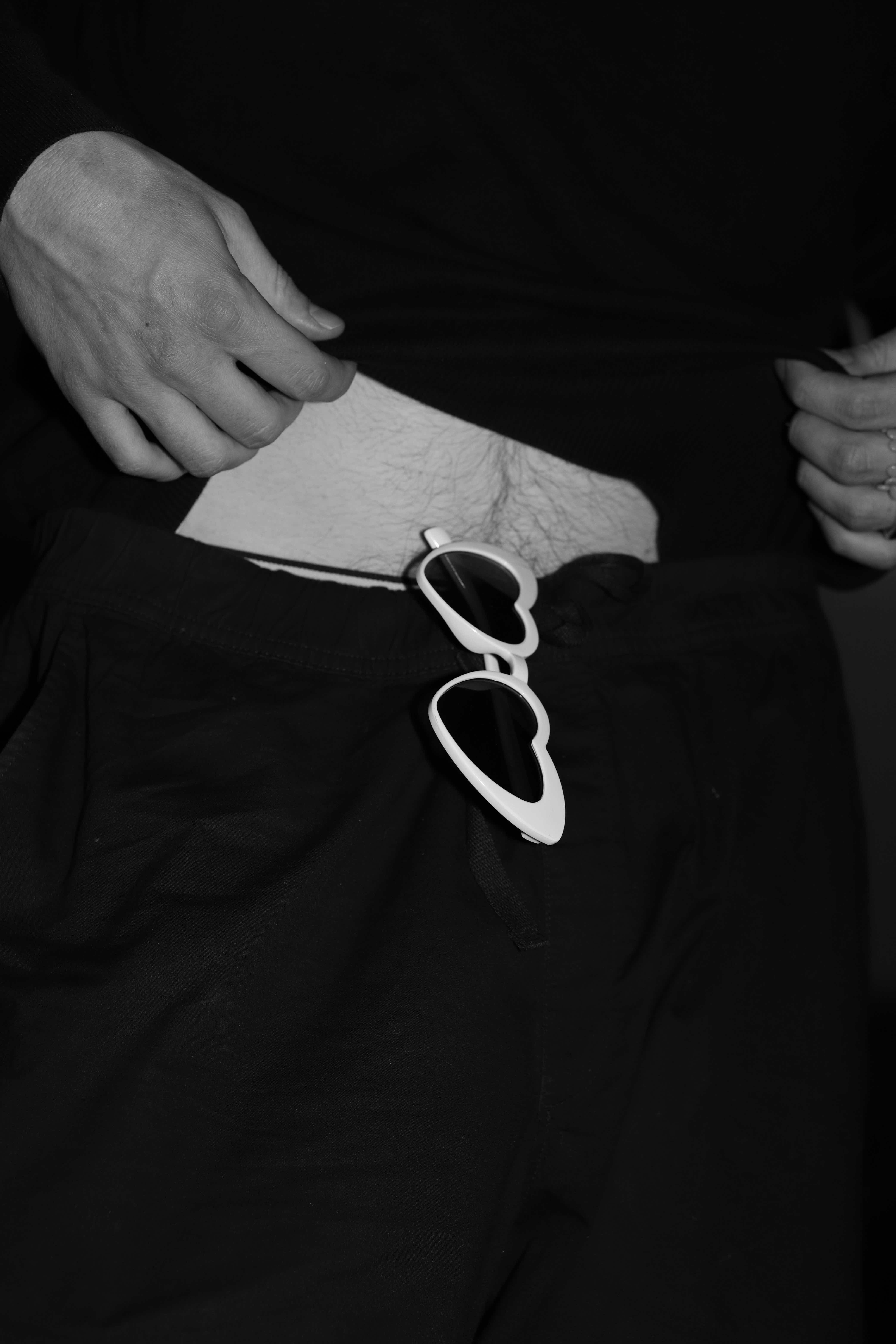  Black and white photograph. Heartshaped sunglasses hanging from the belt of the portrayed. Part of the belly is exposed..
